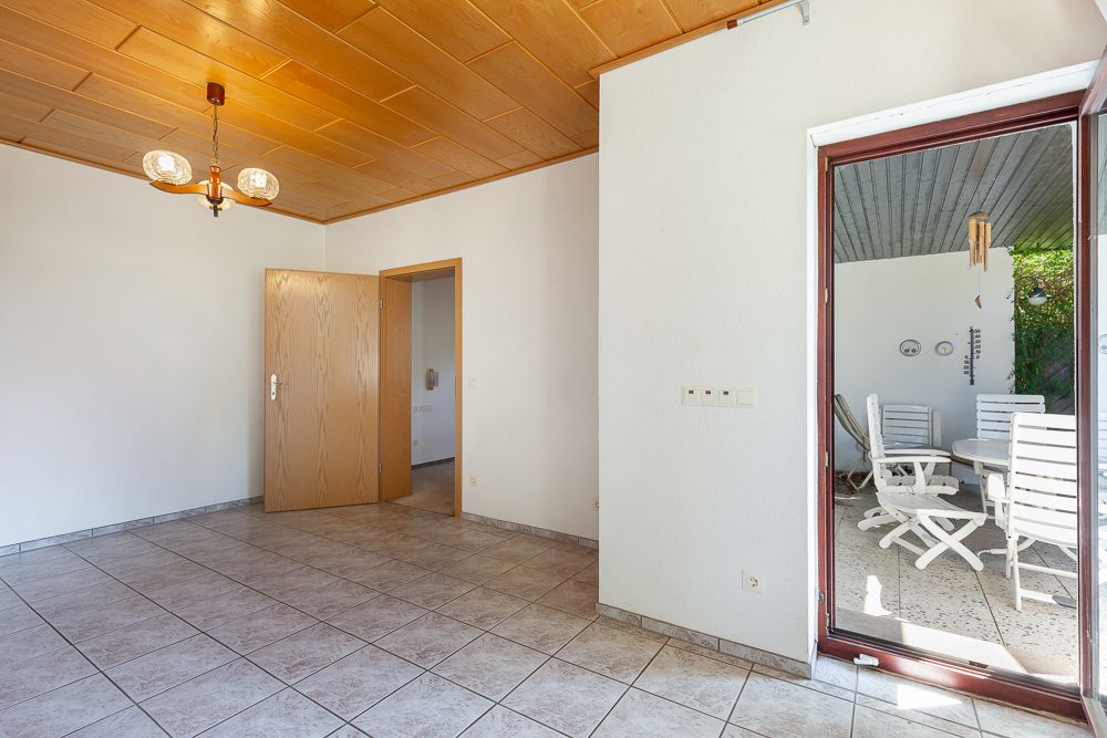 Heller Raum mit Fliesenboden, Holztür, offener Terrasse mit weißen Stühlen und Tisch.