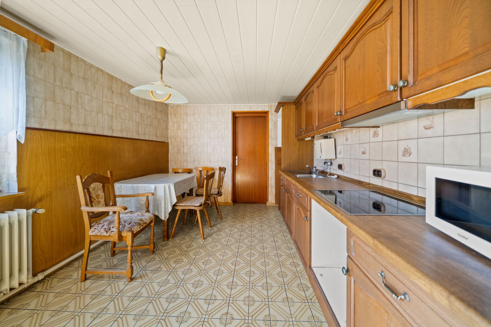 Küche mit Holzmöbeln, Esstisch, vier Stühlen, Fenster und Mikrowelle.