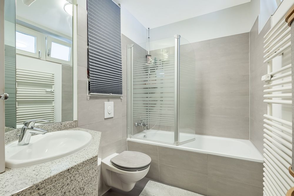 Modernes Badezimmer mit Waschbecken, Toilette, Badewanne, Spiegel und Handtuchheizkörper.