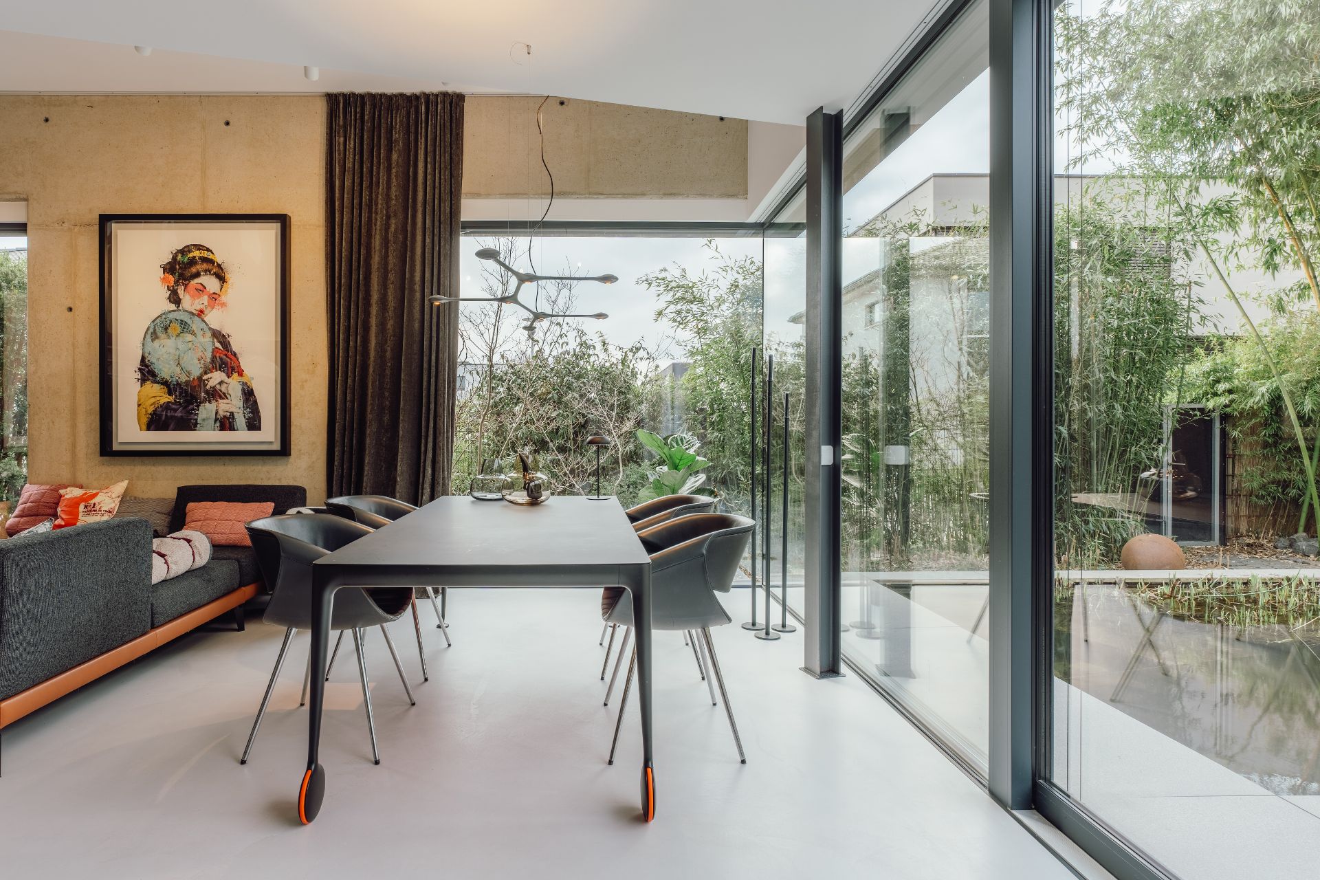 Essbereich mit großem Tisch, Stühlen, Sofa, Kunstwerk und Blick auf Garten durch große Fenster.