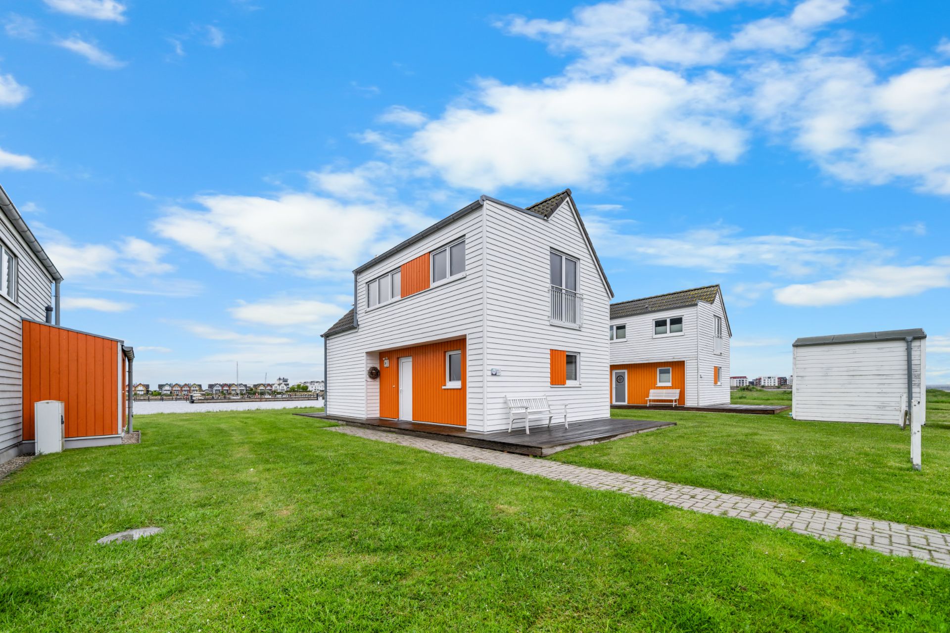 Modernes zweistöckiges Haus mit weißer Fassade und orangefarbenen Akzenten auf einer grünen Rasenfläche.