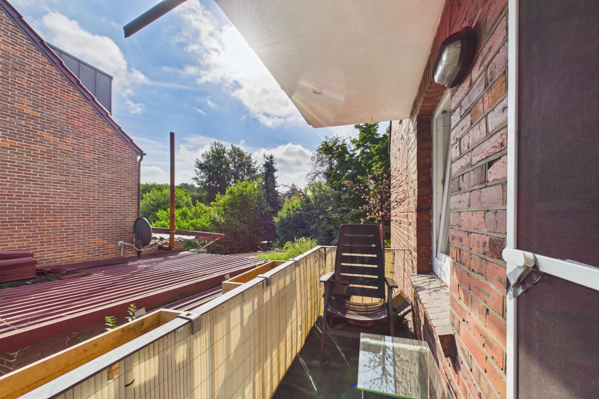 Kleiner Balkon mit Stuhl und Glastisch, Blick auf Garten und Nachbargebäude.