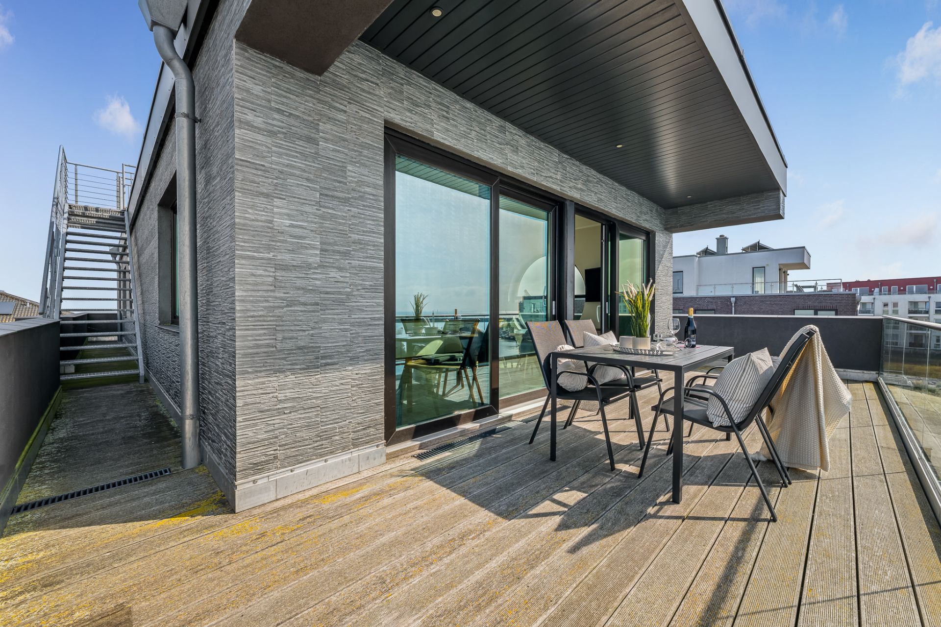 Große Terrasse mit Esstisch, vier Stühlen und Glasgeländer, daneben Treppe nach oben.