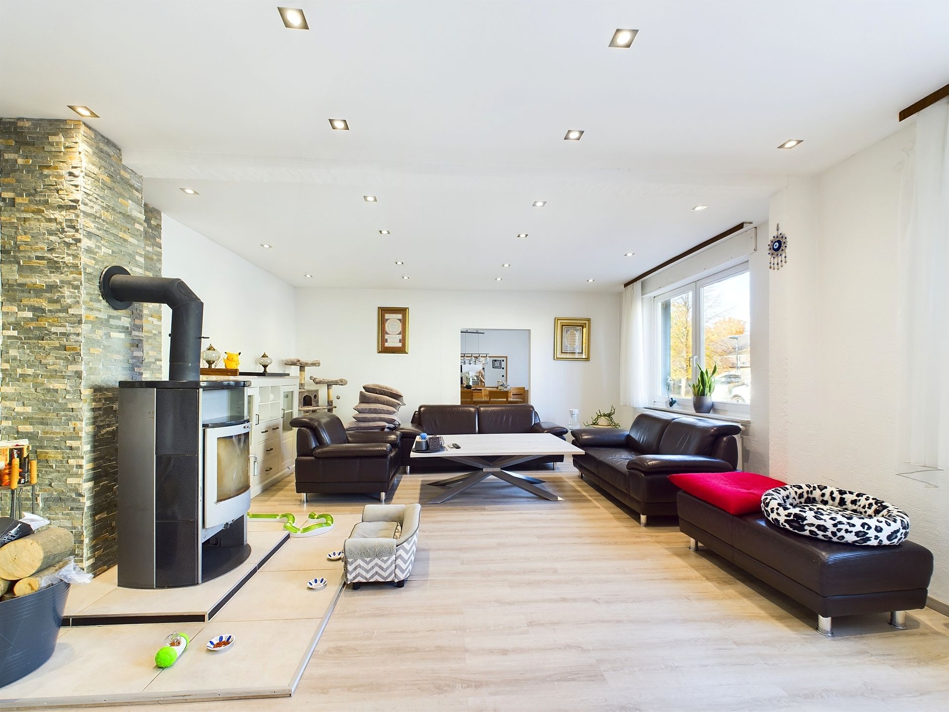 Modernes Wohnzimmer mit Holzofen, dunklen Sofas, Couchtisch und Spielzeug auf hellem Holzboden.