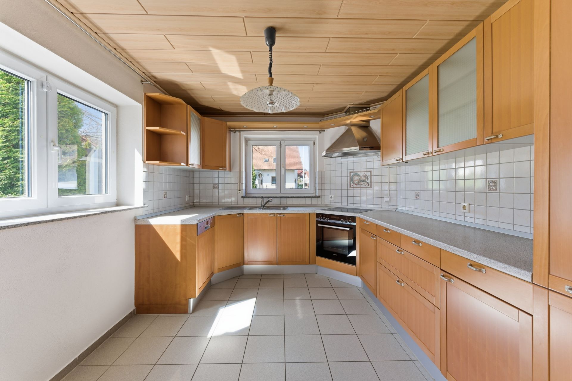 Helle Einbauküche mit Holzfronten, Fliesenboden, Eckspüle und großem Fenster.