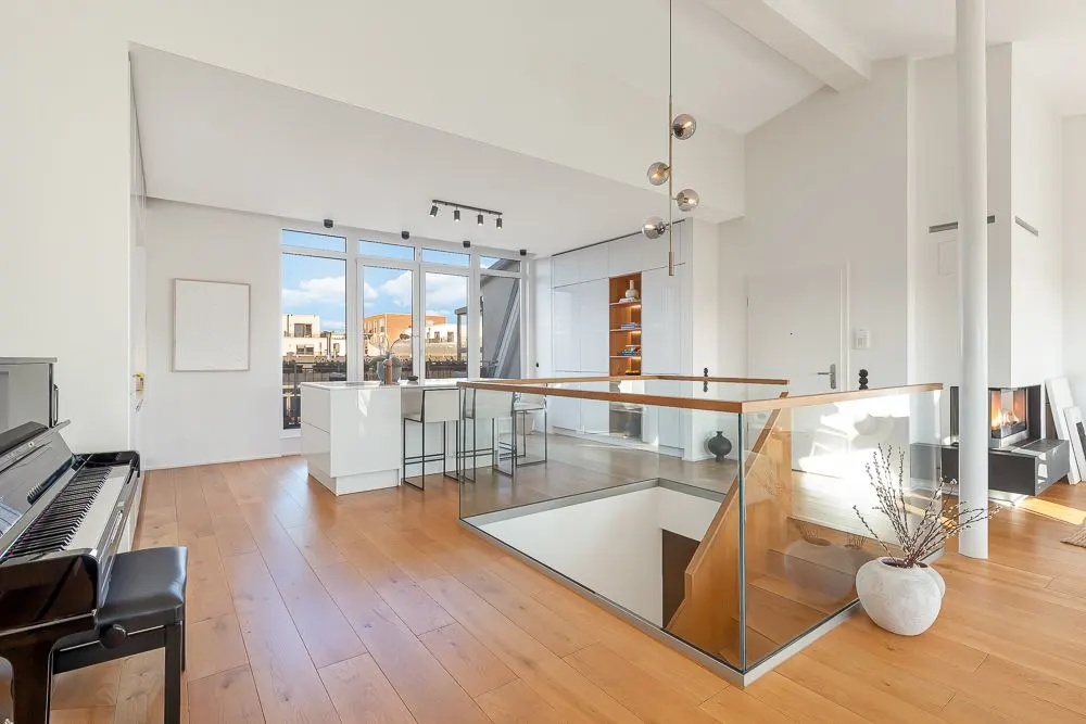 Heller Wohnraum mit Klavier, Holzfußboden, Glasgeländer und großer Fensterfront.