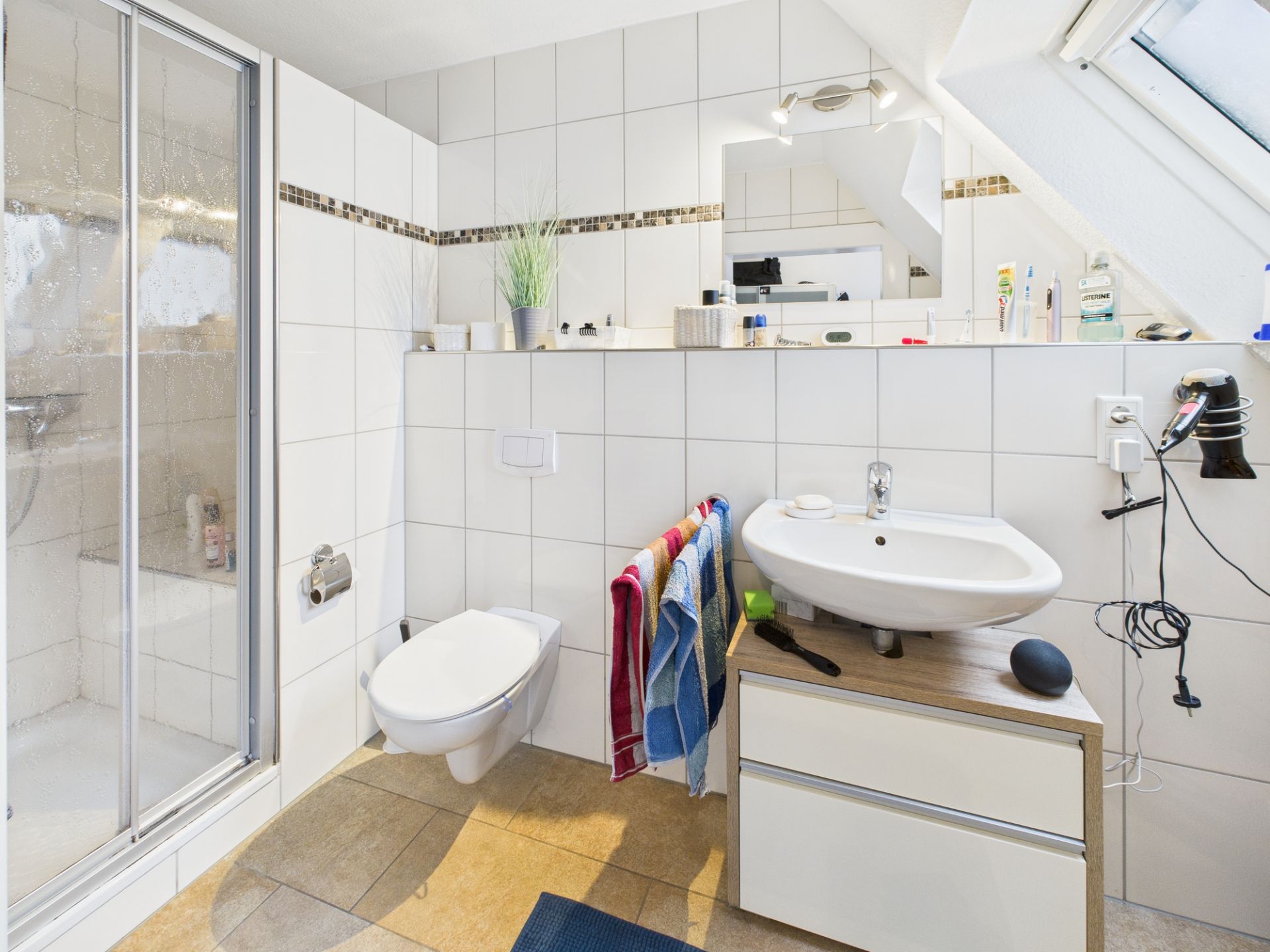 Modernes Badezimmer mit Dusche, WC, Waschbecken, Spiegel und Handtüchern an der Wand.