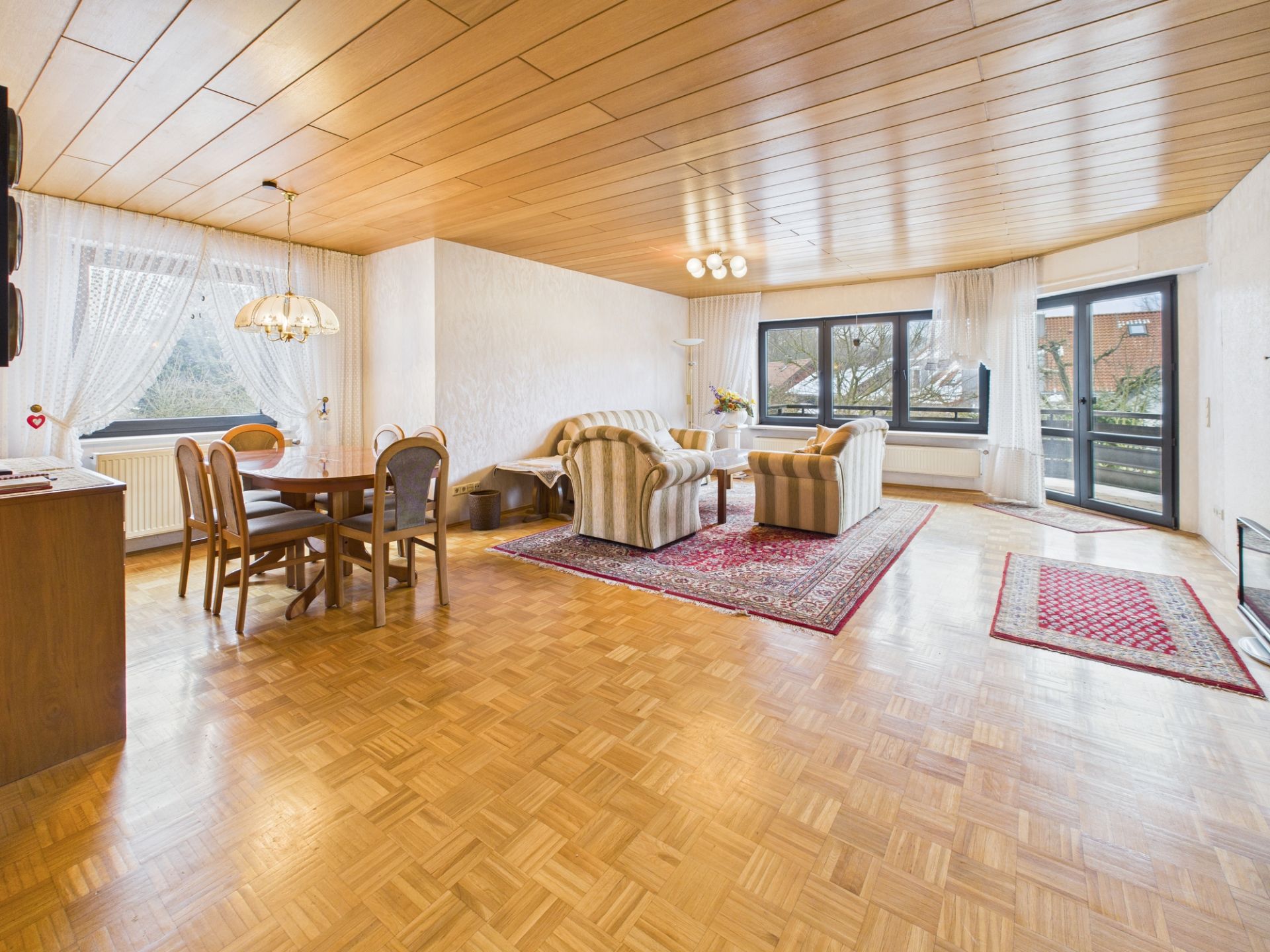 Helles Wohnzimmer mit Parkettboden, Essbereich, Sofas, Teppichen und großen Fenstern.