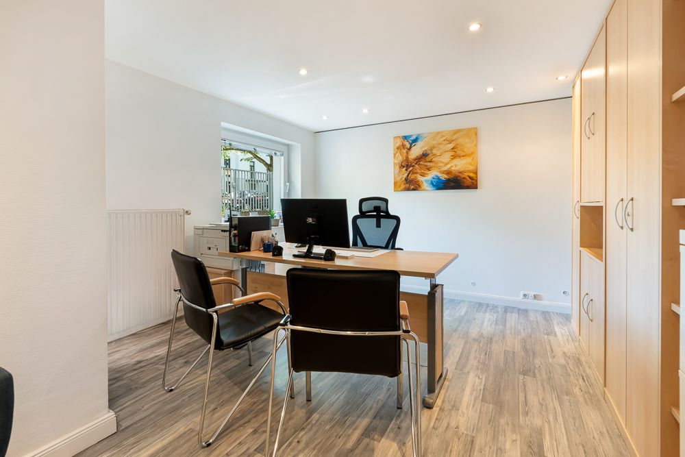 Modernes Arbeitszimmer mit großem Schreibtisch, zwei Stühlen und Regalen. Fenster sorgt für Tageslicht.