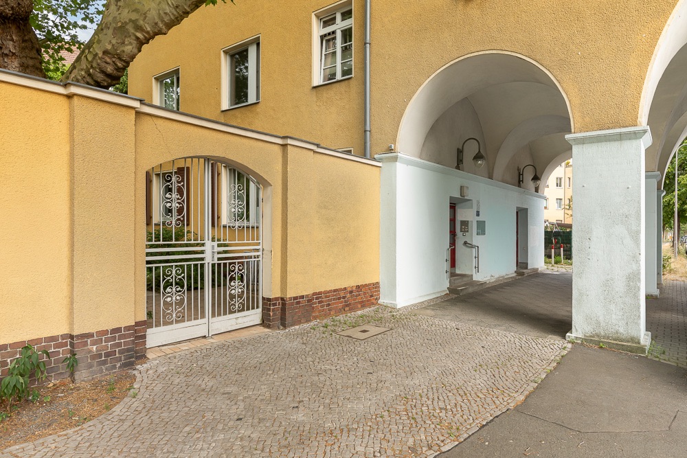 Gelbes Wohnhaus mit Tor, Rundbögen und gepflastertem Gehweg.