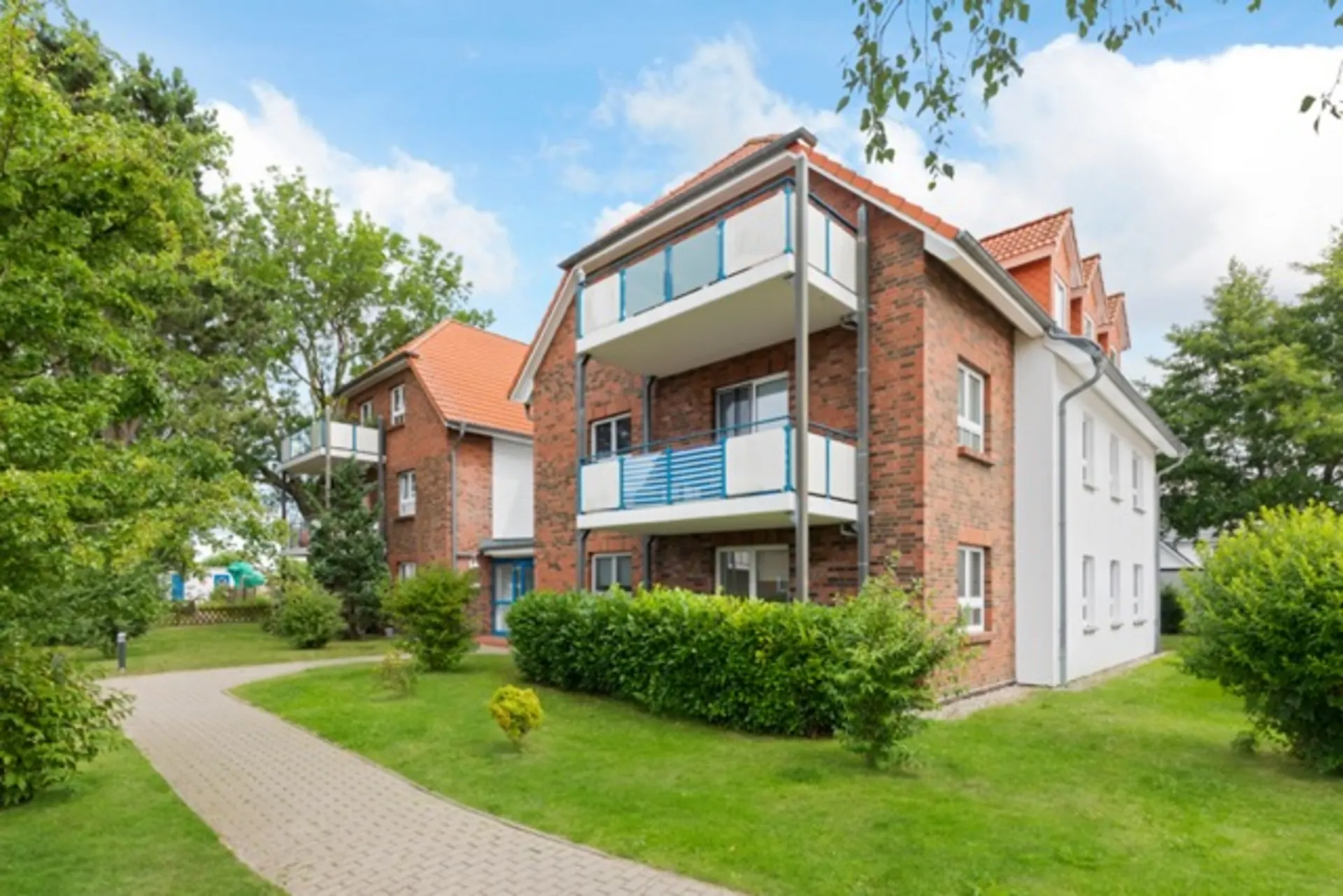 Zweistöckiges Wohnhaus aus Backstein mit Balkonen, umgeben von Garten und Weg.