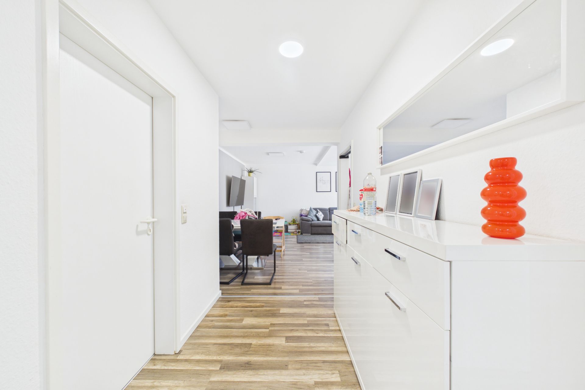 Heller Flur mit weißem Sideboard, Spiegel und Blick ins Wohnzimmer mit Sofa und Esstisch.