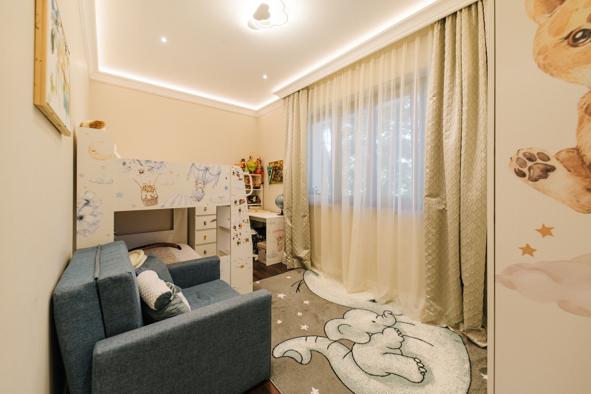 Kinderzimmer mit Hochbett, Sofa, Schreibtisch und Vorhängen vor einem Fenster.