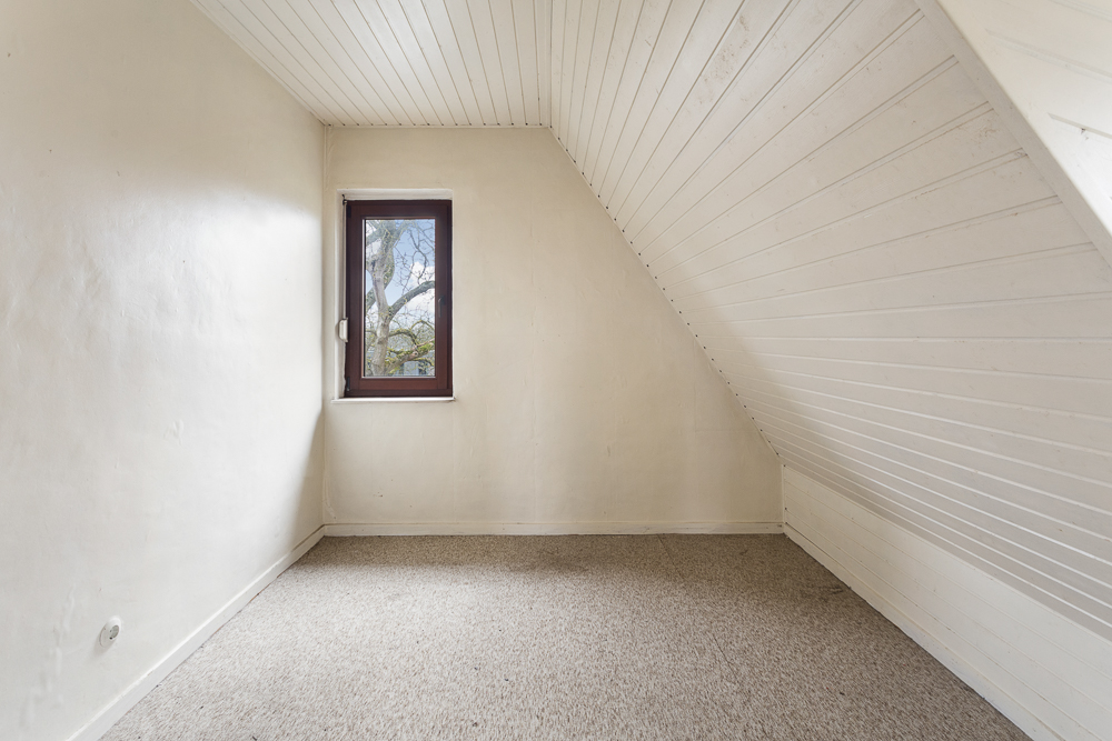 Kleiner leerer Raum mit schräger Holzdecke und einem Fenster an der Stirnwand.