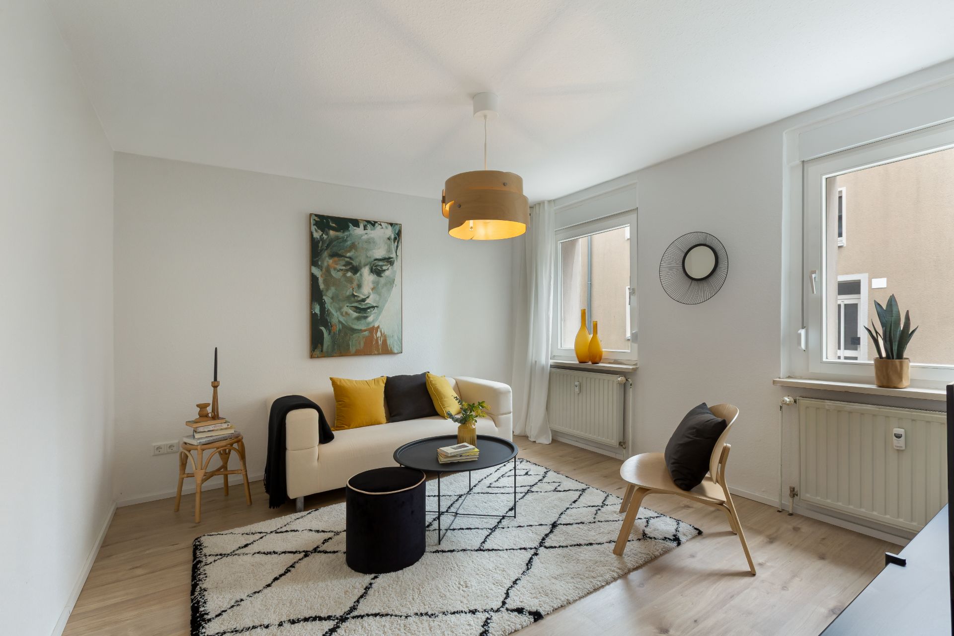 Modernes Wohnzimmer mit Sofa, Teppich, zwei Fenstern und Wandbild.