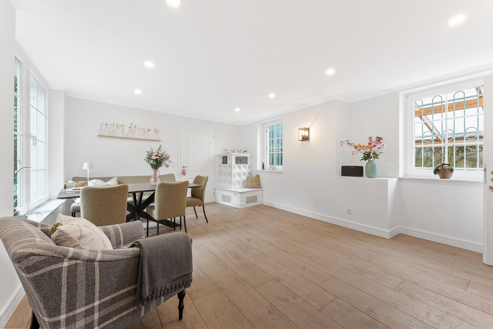 Helles Wohnzimmer mit Esstisch, vier Stühlen, Sessel und Dekoration auf Holzboden.