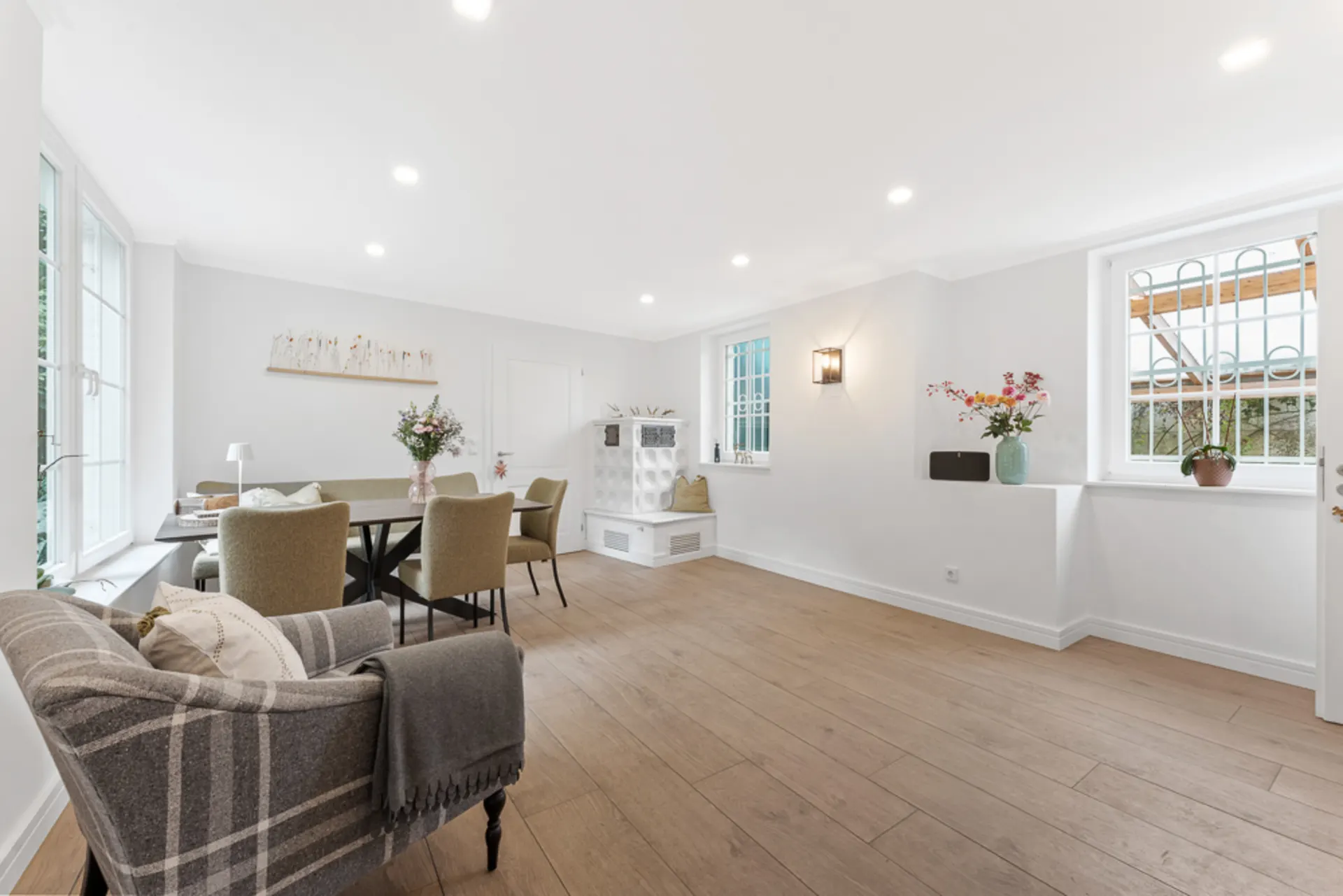 Helles Wohnzimmer mit Esstisch, vier Stühlen, Sessel und Dekoration auf Holzboden.