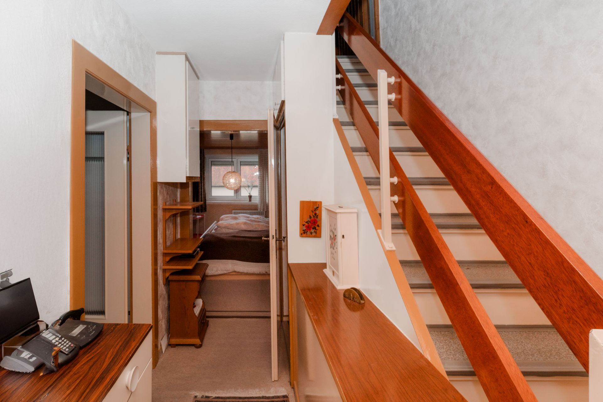 Flur mit Treppe, Telefon auf einem Schrank und Blick in ein Schlafzimmer.
