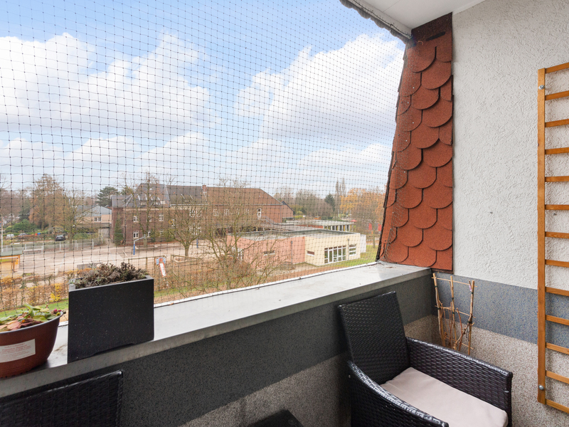 Balkon mit Netz, Blick auf Häuser und Bäume, zwei Stühle und einige Pflanzen.