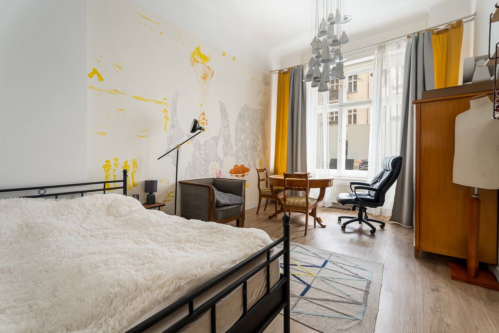 Helles Zimmer mit Bett, Sessel, Tisch, Schreibtischstuhl, Kleiderschrank und großem Fenster.