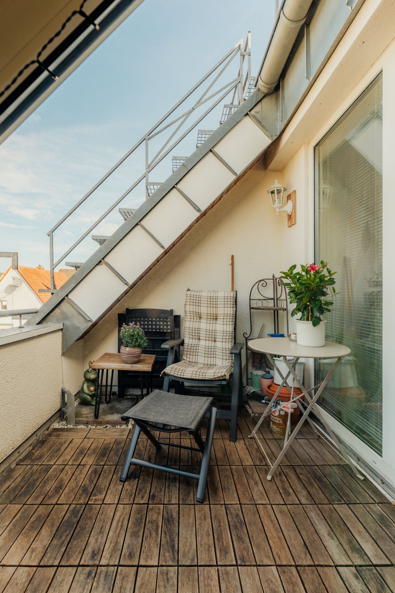 Kleine Terrasse mit Holzfußboden, Stuhl, Tisch, Pflanzen und Metalltreppe.