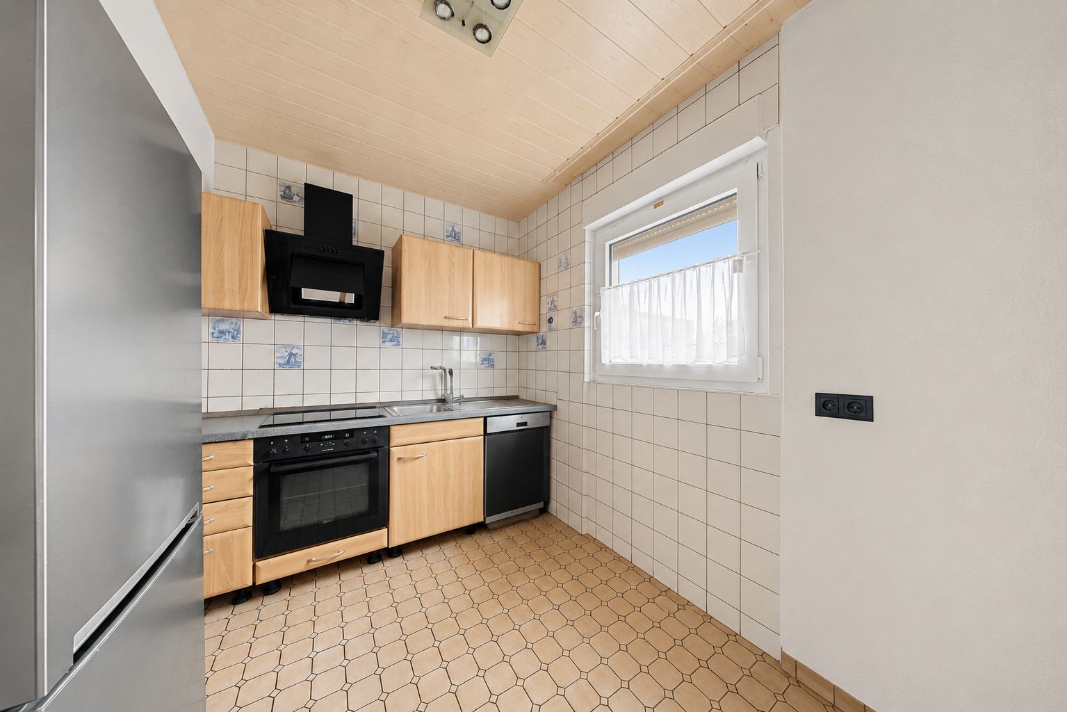 Kleine Küche mit Holzmöbeln, weiß gefliesten Wänden, Fenster und modernen Geräten.