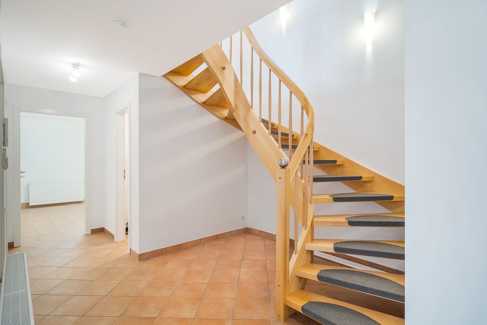Heller Flur mit gefliesten Boden und Holztreppe, die ins Obergeschoss führt.