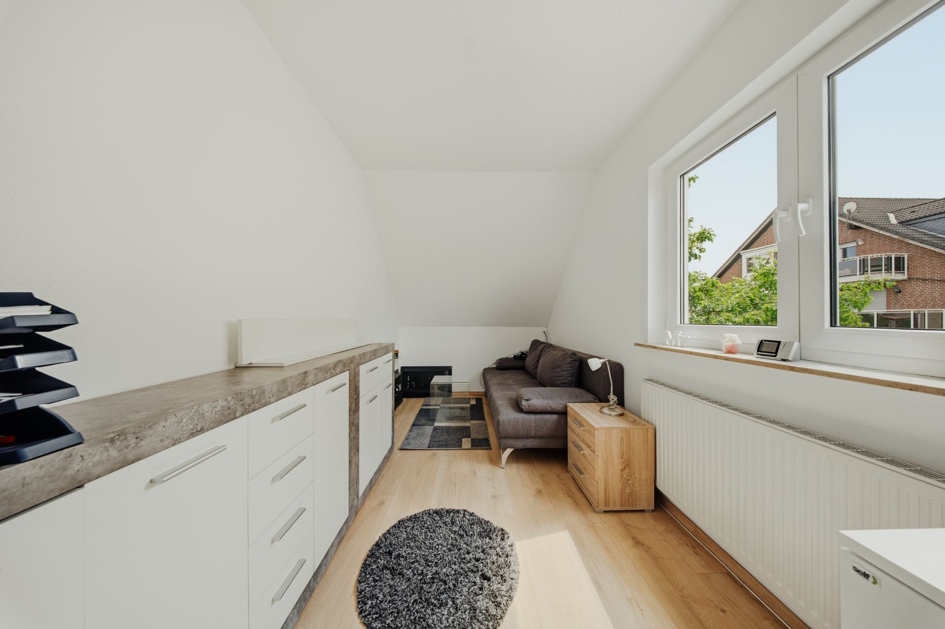 Helles Wohnzimmer mit Sofa, Teppich, Fenster und Sideboard auf Holzfußboden.