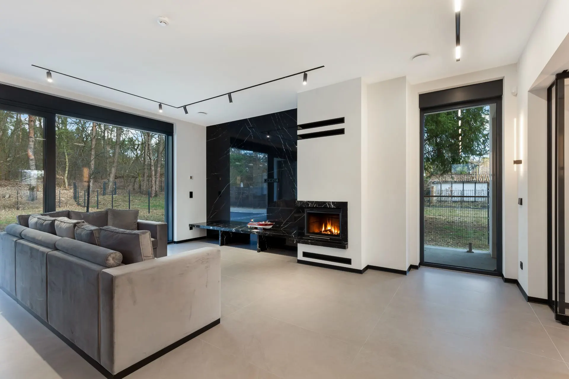 Modernes Wohnzimmer mit grauem Sofa, großem Fenster, Kamin und Blick auf den Garten.