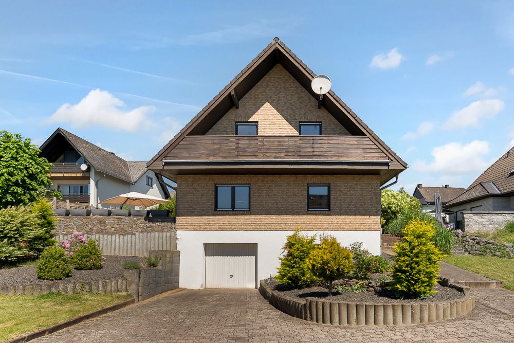 Vorderansicht eines Einfamilienhauses mit Garten, Einfahrt und Garage.