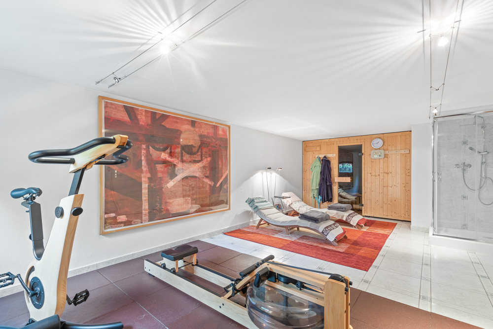 Fitnessbereich mit Ergometer, Rudergerät, zwei Liegen, Sauna und Dusche in einem Raum.