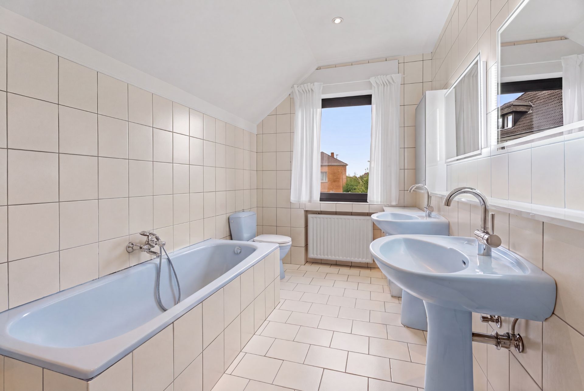 Helles Bad mit Badewanne, zwei Waschbecken, Toilette und großem Fenster.
