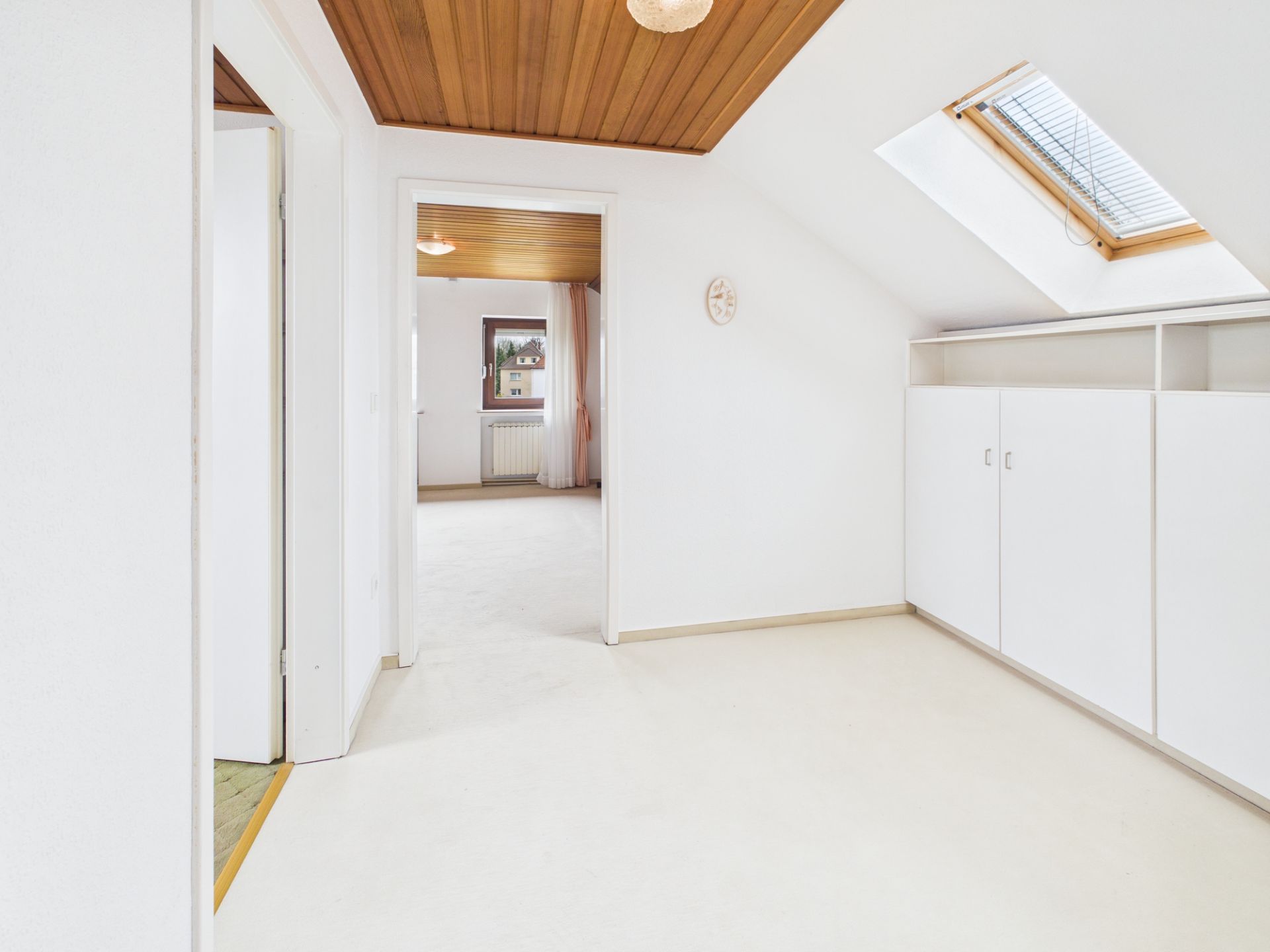 Heller Raum mit Holzdecke, Dachfenster und weißen Einbauschränken.
