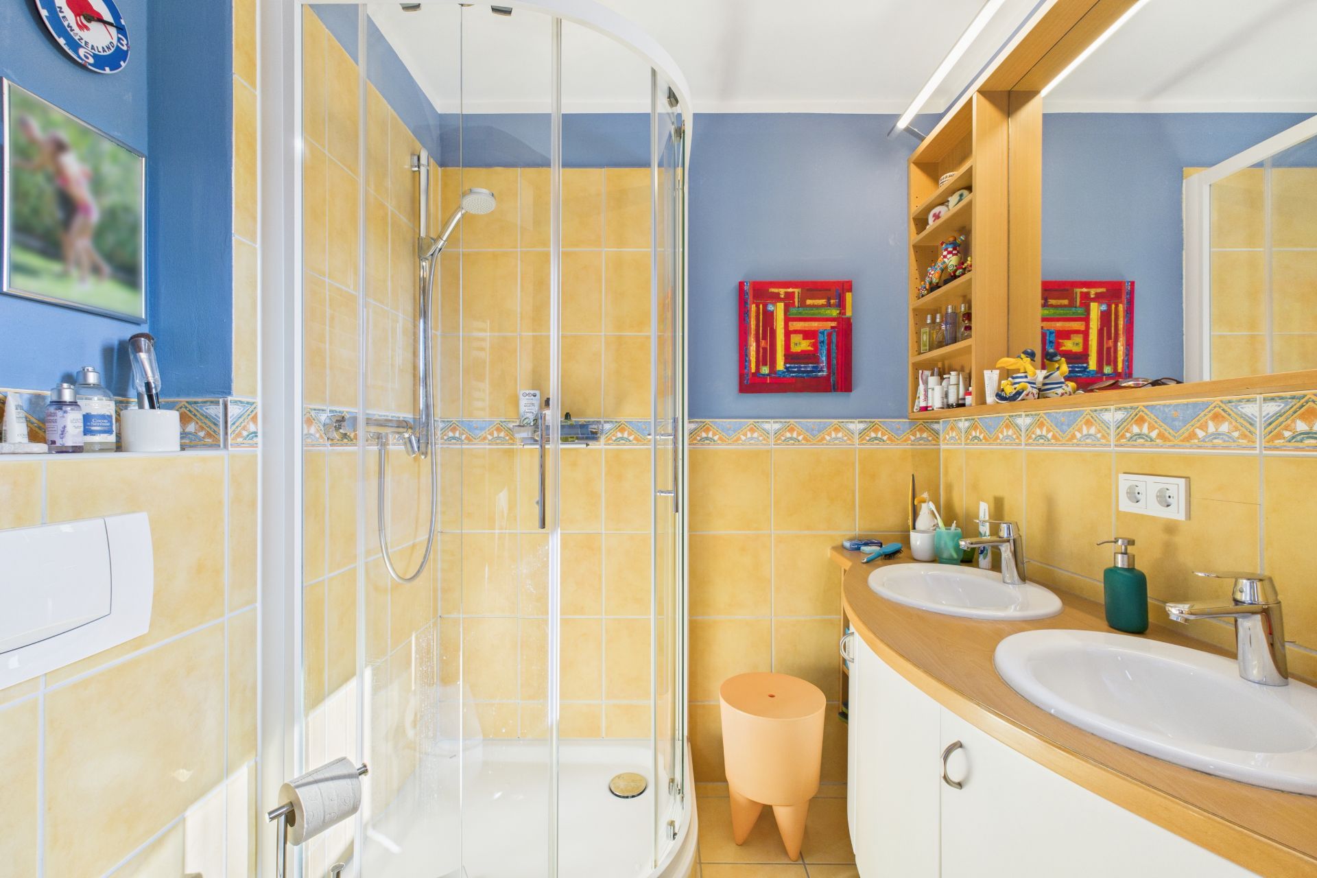 Modernes Badezimmer mit Dusche, zwei Waschbecken und gelb-blauen Fliesen.