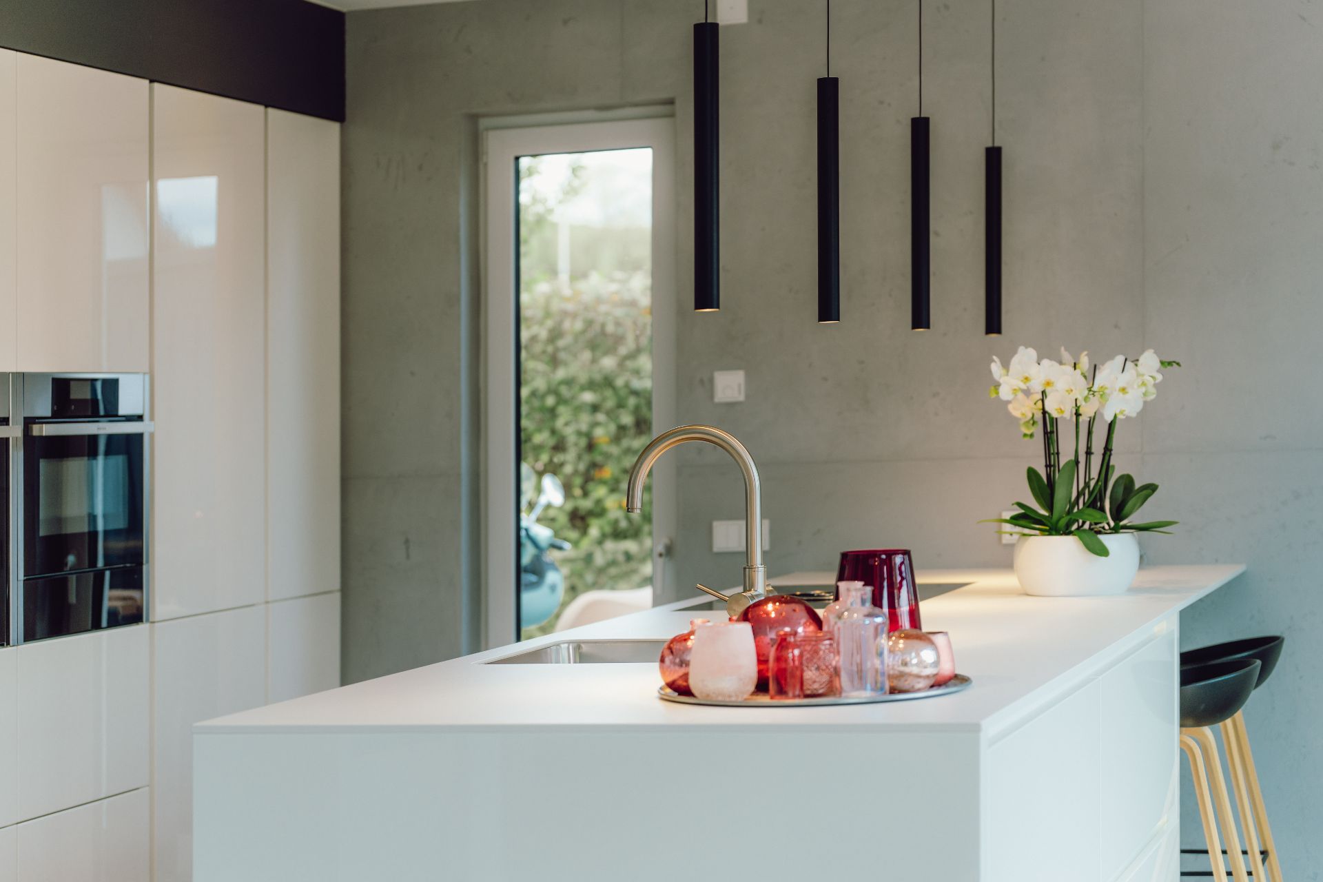 Moderne Küche mit Kochinsel, Hockern, Hängelampen und Orchidee im weißen Topf.