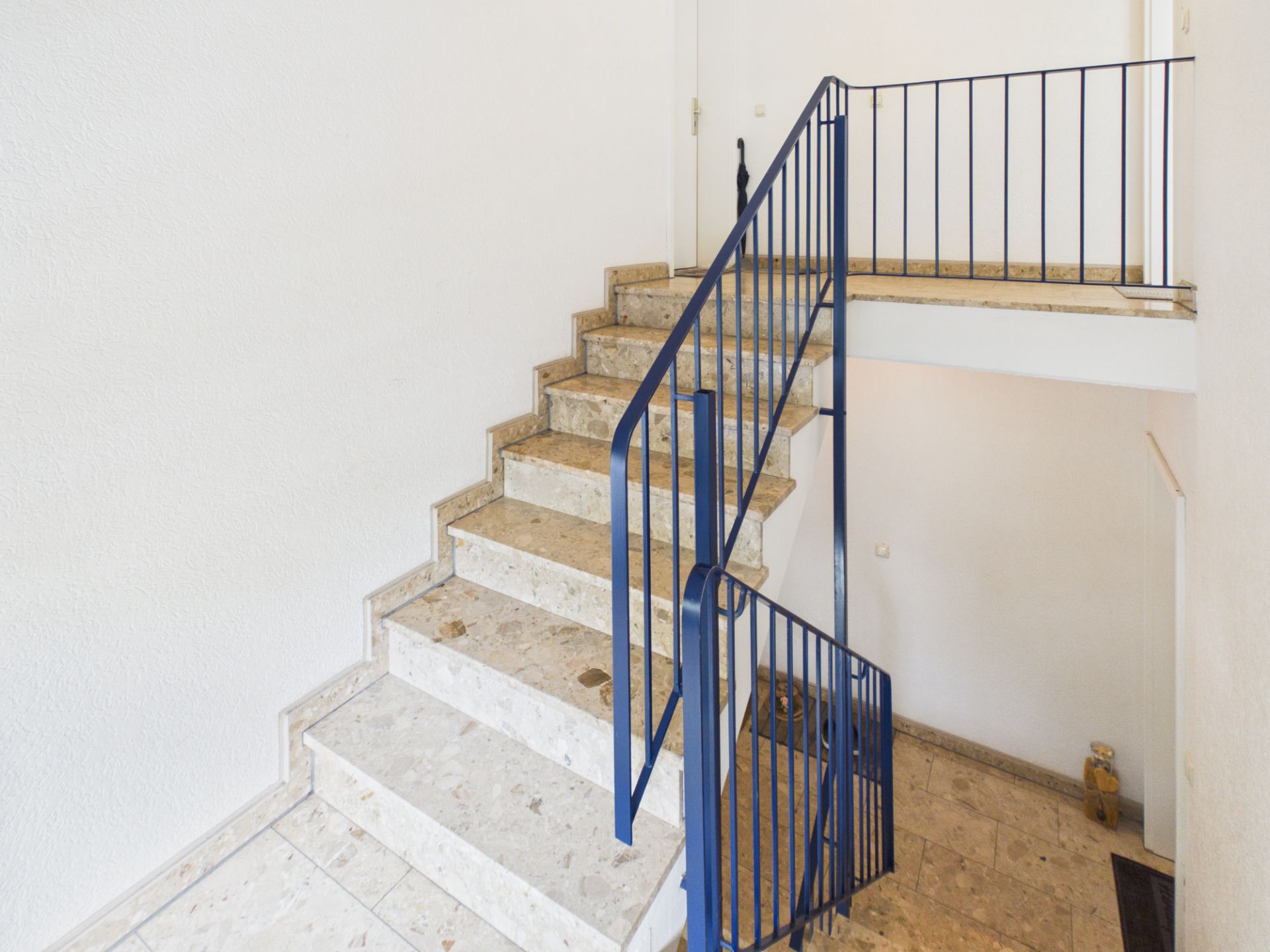 Helle Innentreppe mit Marmorstufen und blauem Geländer in einem Wohnhaus.