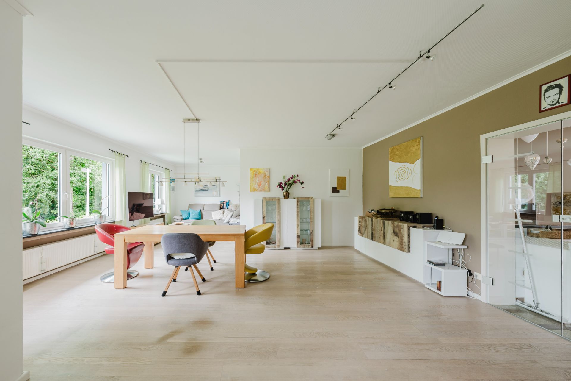 Helles Wohnzimmer mit großem Esstisch, bunten Stühlen und großen Fenstern.