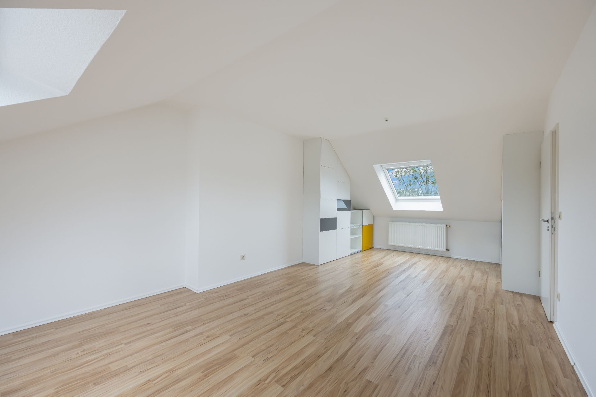 Heller Raum mit Holzfußboden, weißer Wand, Dachfenster und Heizung unter dem Fenster.