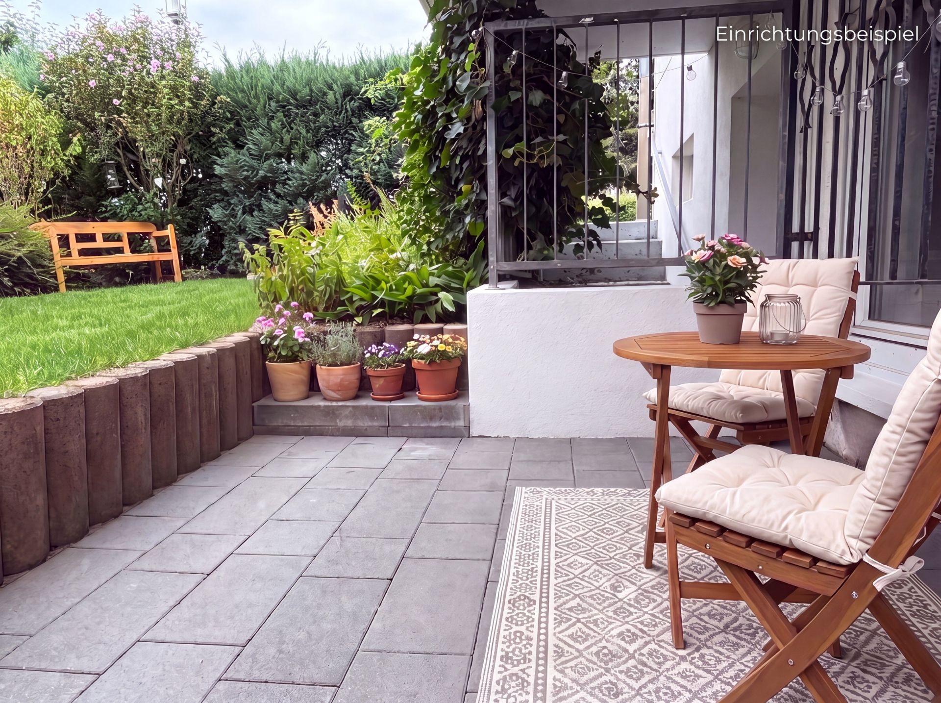 Terrasse mit Holztisch, zwei Stühlen, Blumentöpfen und Gartenbank im Hintergrund.
