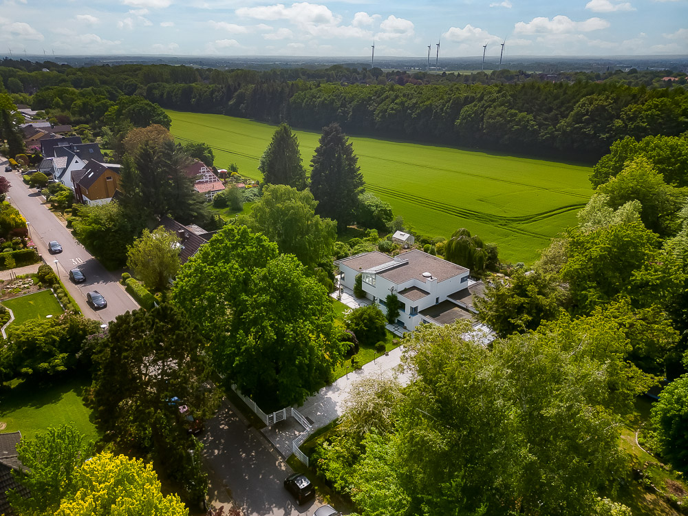 Luftaufnahme eines Wohnhauses mit Garten am Rand einer grünen Wiese und Bäumen.