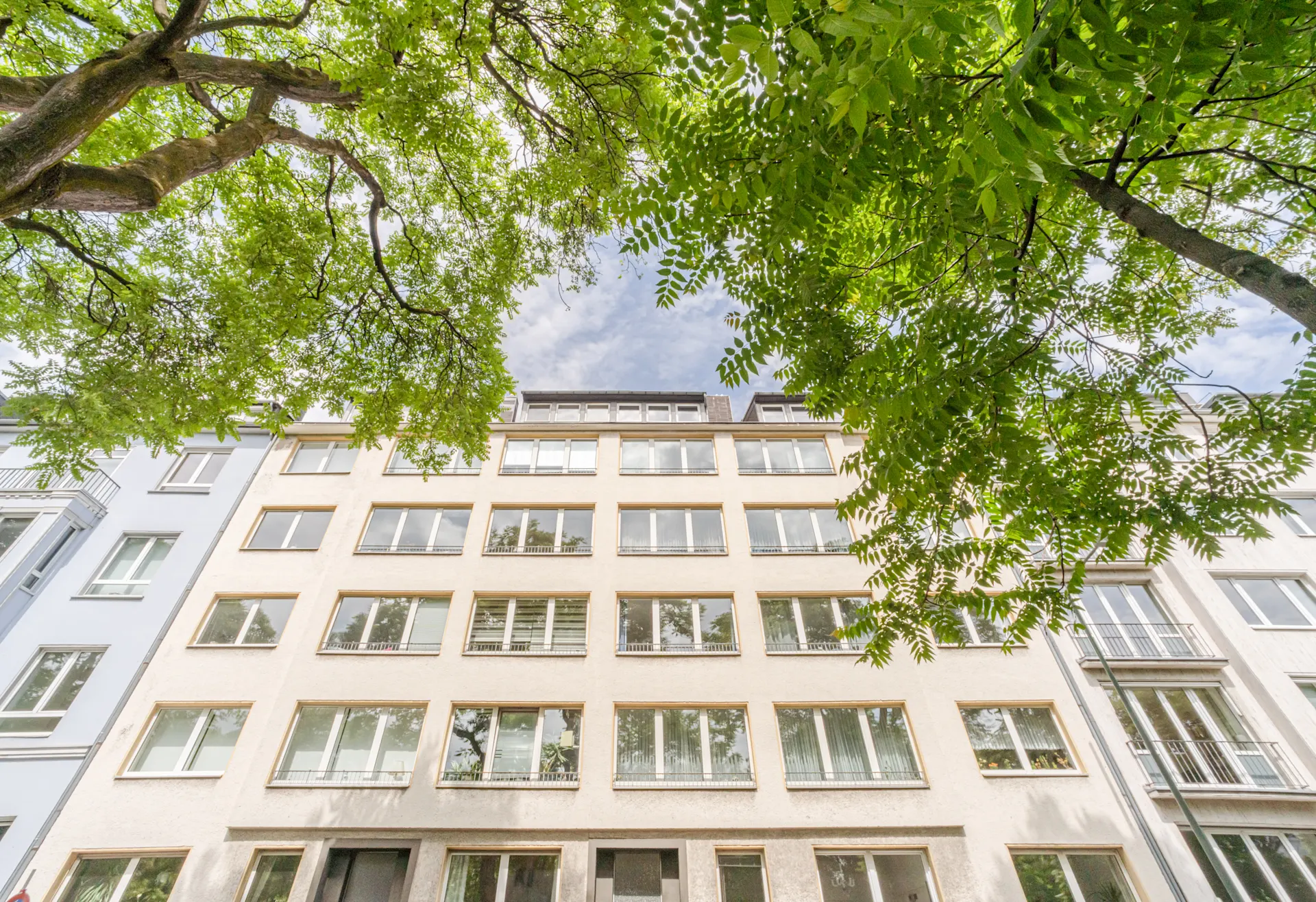 Mehrstöckiges Wohngebäude mit vielen Fenstern und Bäumen im Vordergrund.