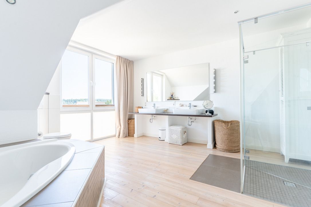 Helles Badezimmer mit Badewanne, Dusche, Doppelwaschbecken und großen Fenstern.