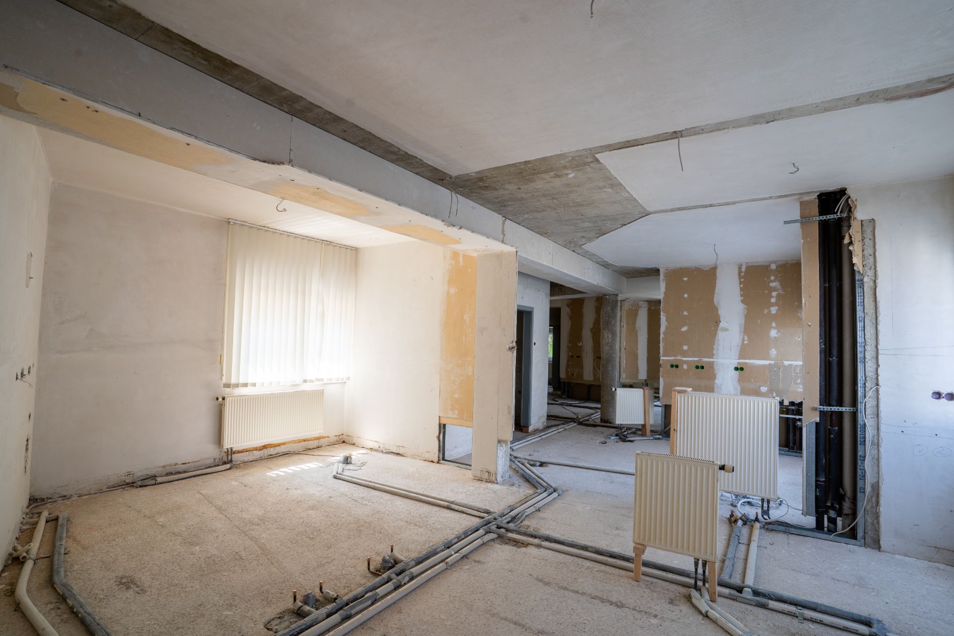 Renovierter Raum mit sichtbaren Heizkörpern, Rohren und abgestreiften Wänden.