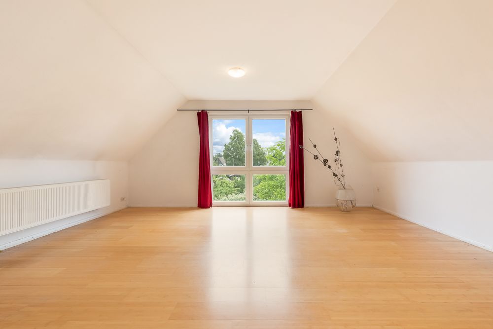 Heller, leerer Raum mit Holzfußboden, großem Fenster, roten Vorhängen und Dekovase.