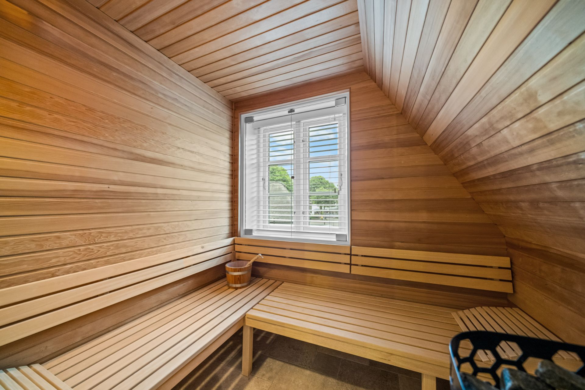Holzsauna mit zwei Bänken, Eimer auf der Bank und Fenster mit Blick nach draußen.