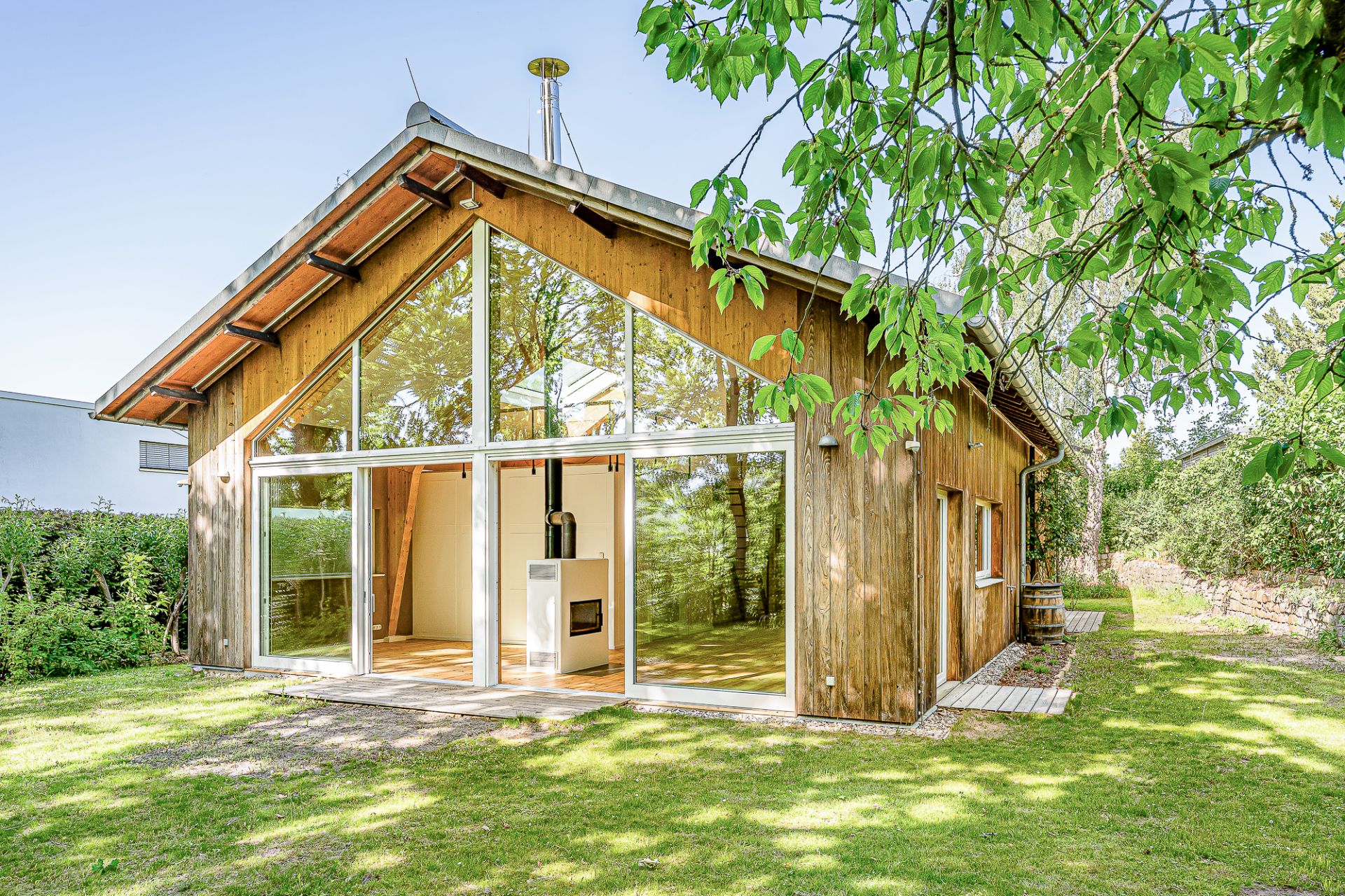 Modernes Holzhaus mit großer Glasfront und Terrasse, umgeben von Rasen und Bäumen.