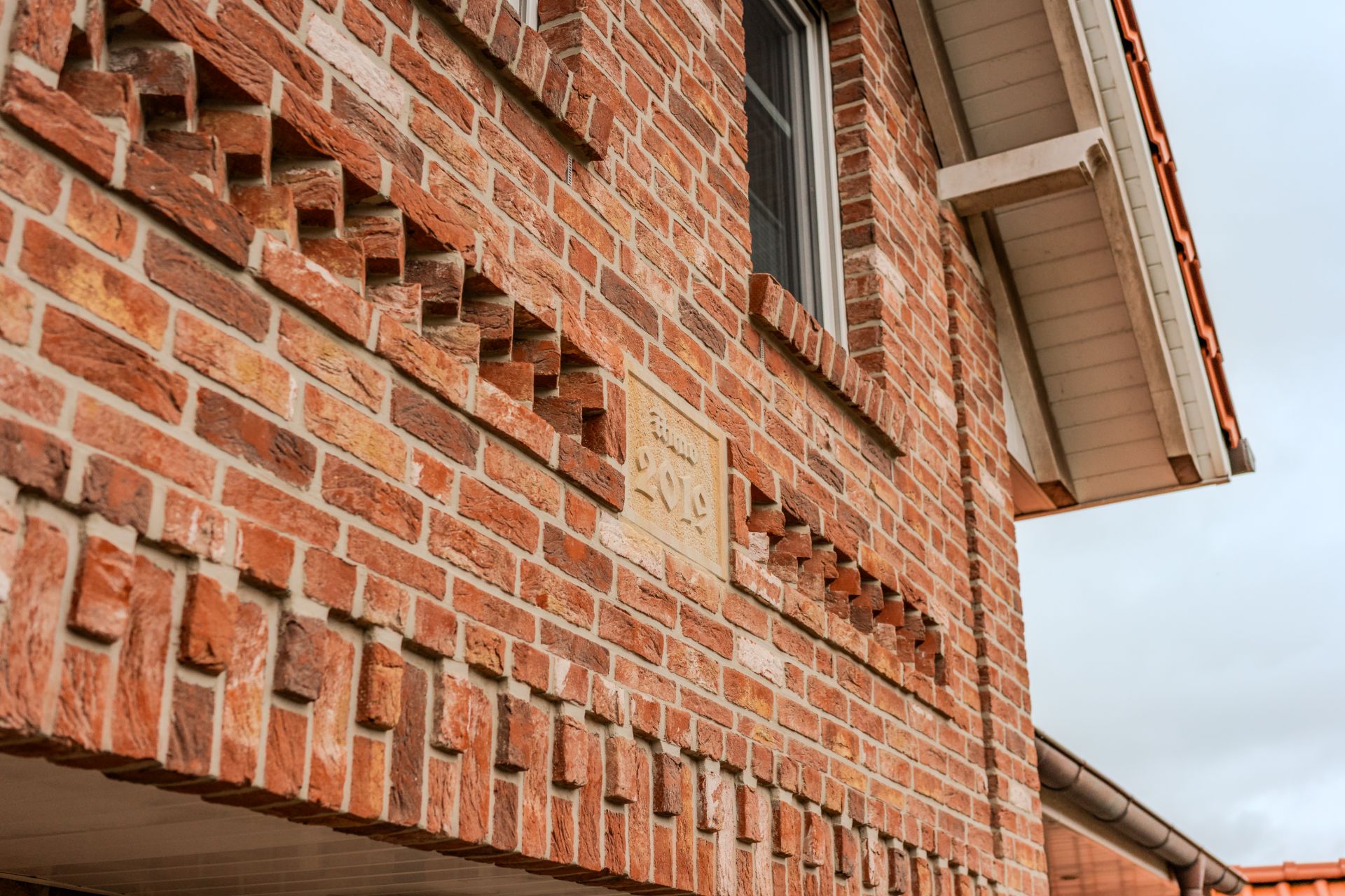 Rote Ziegelsteinfassade eines Hauses mit Fenster und dekorativen Mauersteinen.