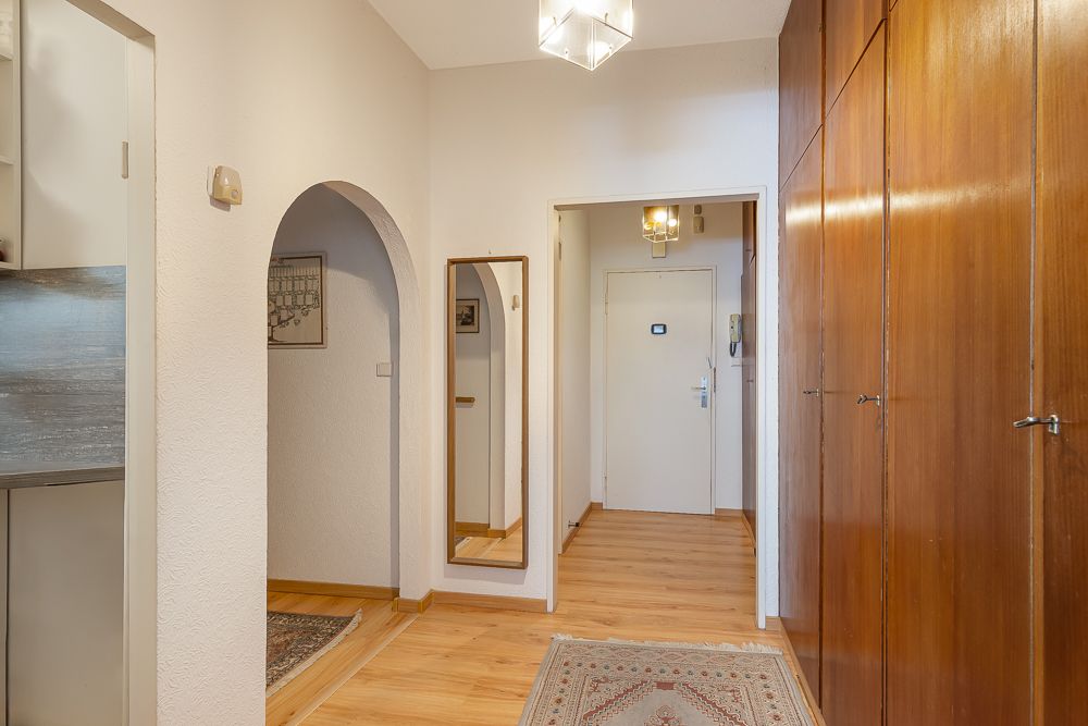 Heller Flur mit Holzschränken, Spiegel, Teppich und Sicht auf weiße Eingangstür.