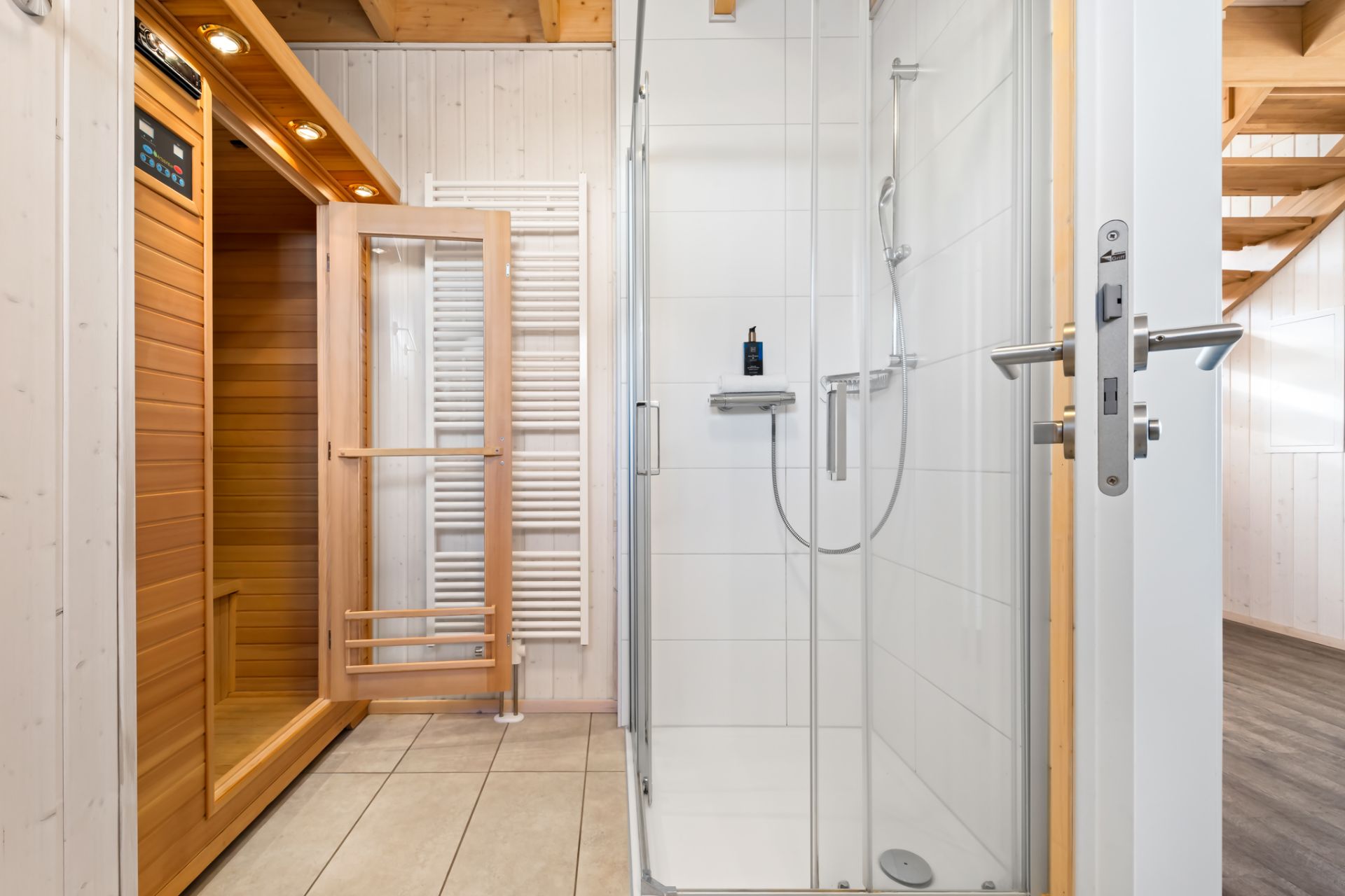 Moderne Dusche und Holzsauna in einem hellen Badezimmer mit Fliesenboden.
