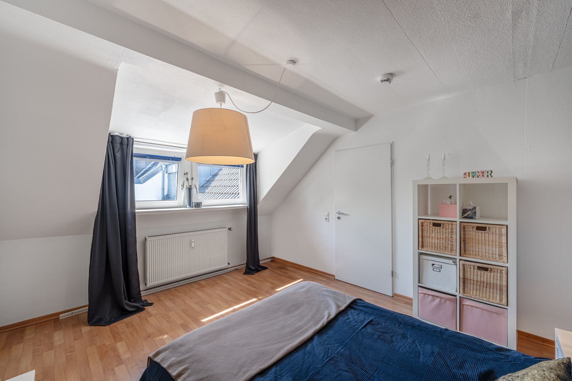 Helles Schlafzimmer mit Dachfenster, Holzboden, Regal und Bett.